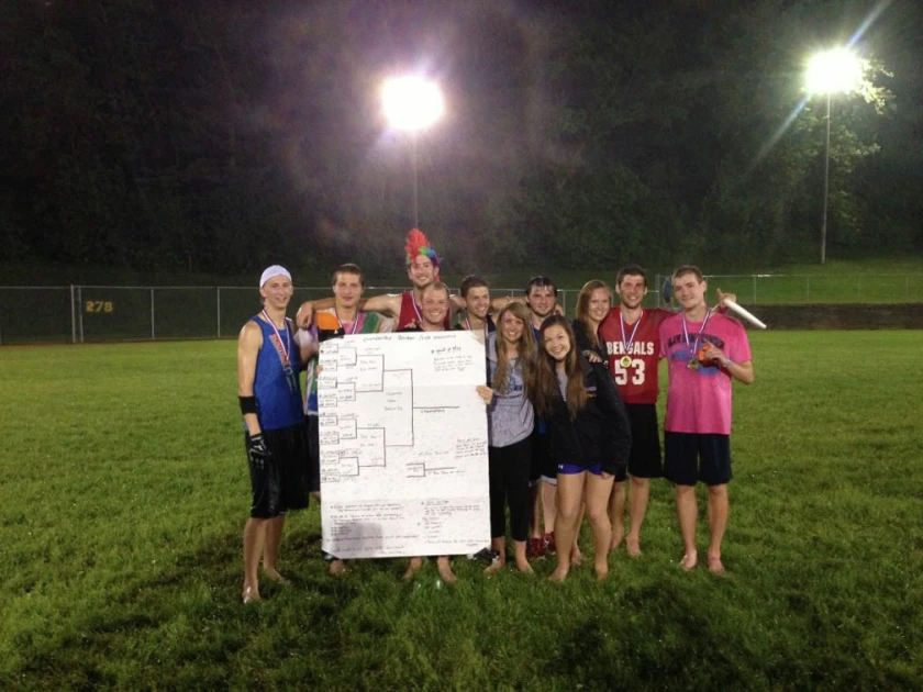 A team with medals posing at night with a giant hand-drawn tournament bracket