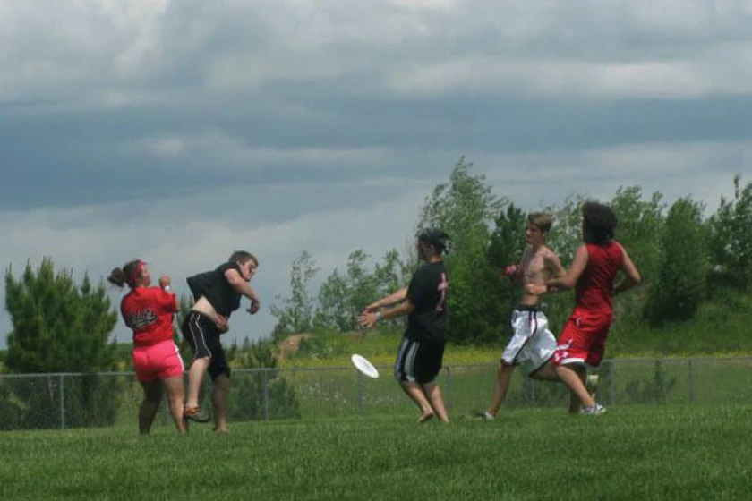 Players chasing a disc across a grass field under a cloudy summer sky